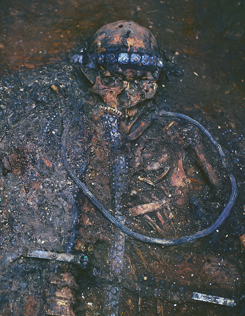 Close view of the burial during the excavation, 1981. The electrum belt is put around the neck of the deceased as a sign of submission to gods. On the waist is one of Crusader belts. Also discernable compositions of embroidery and metal plaques, decorating the loros kaftan and the inner tunic. The photograph demonstrates impressively meticulous work of the archeologists. (source: V. I. Klochko)